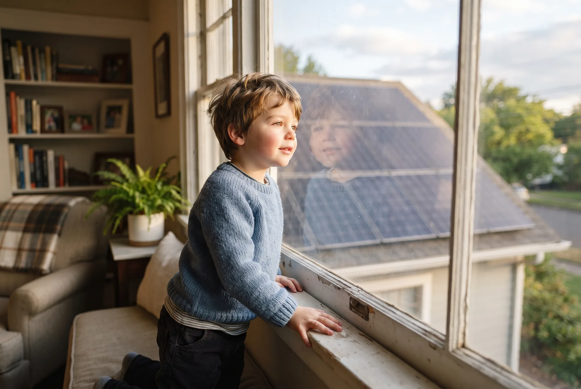 Child looking through a window toward solar panels on a nearby roof